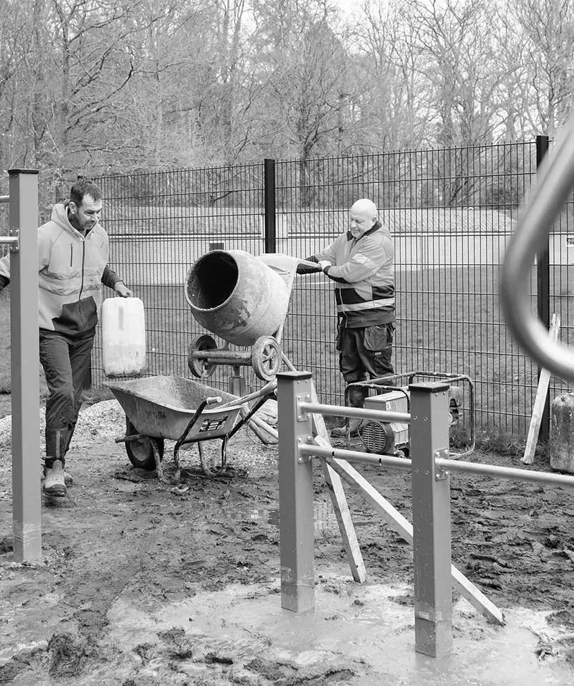 Two men using a concrete mixer during a playground installation.